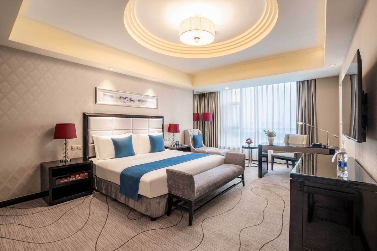 Una habitación de hotel con una cama grande, mesitas de noche, un escritorio, una silla y un televisor.