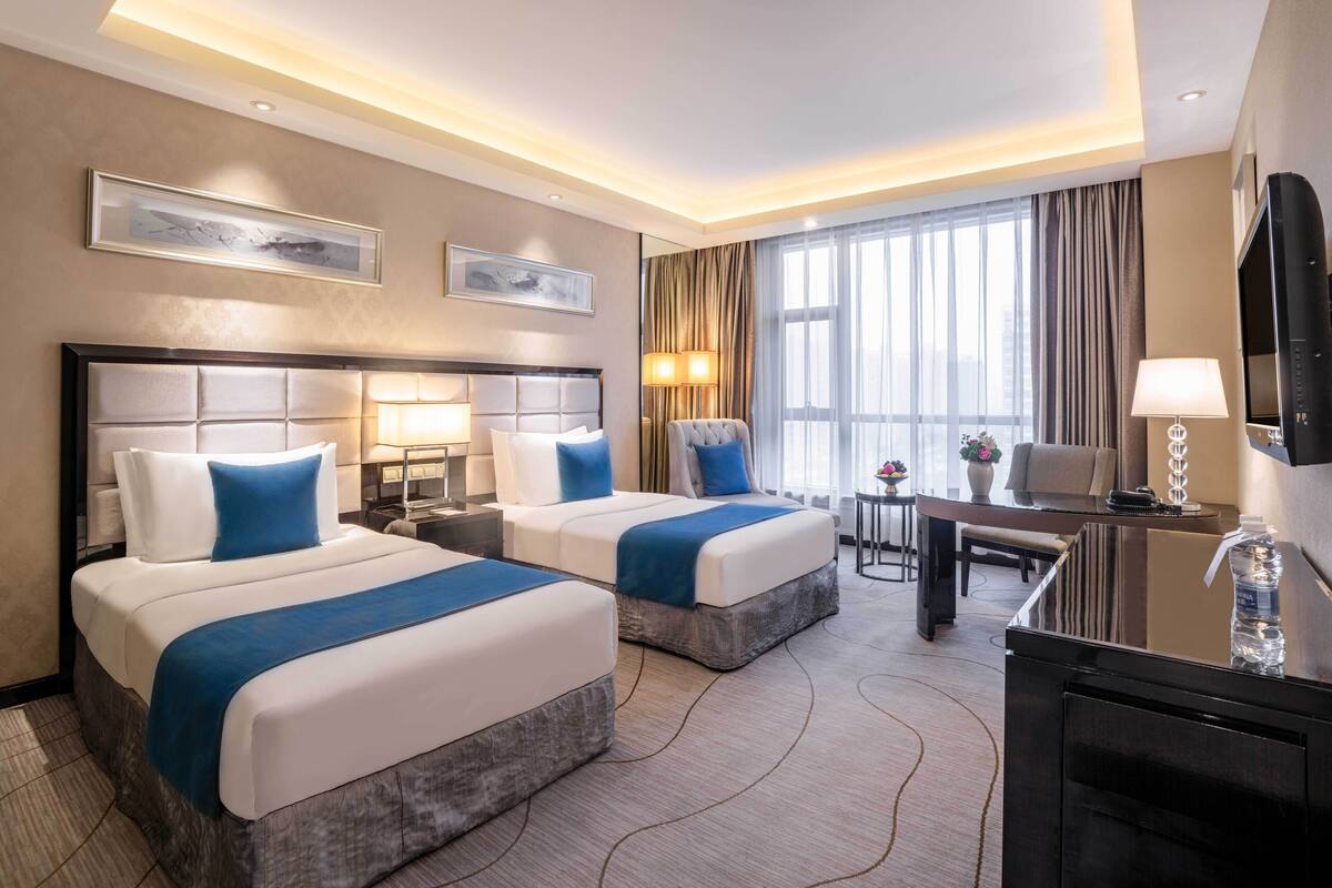 Habitación de hotel con dos camas, un escritorio, un televisor y un ventanal con cortinas.