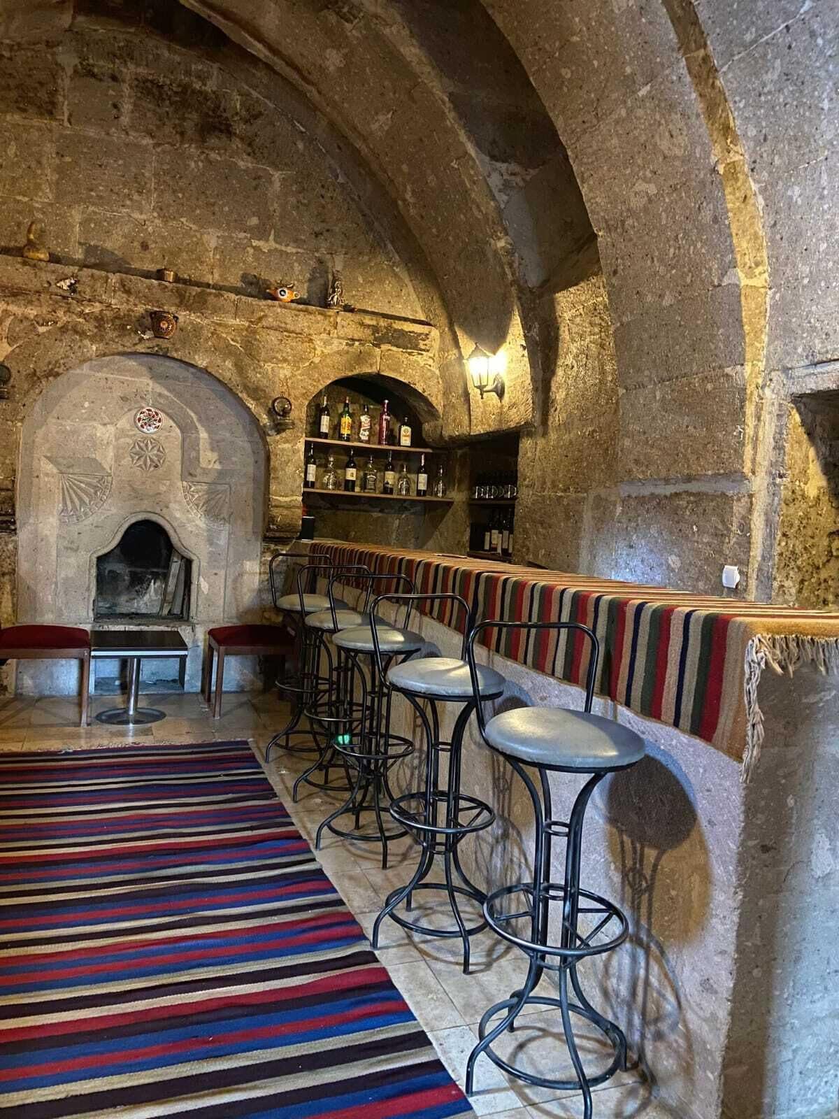 A bar area with stone walls, a fireplace, and a bar counter with stools.