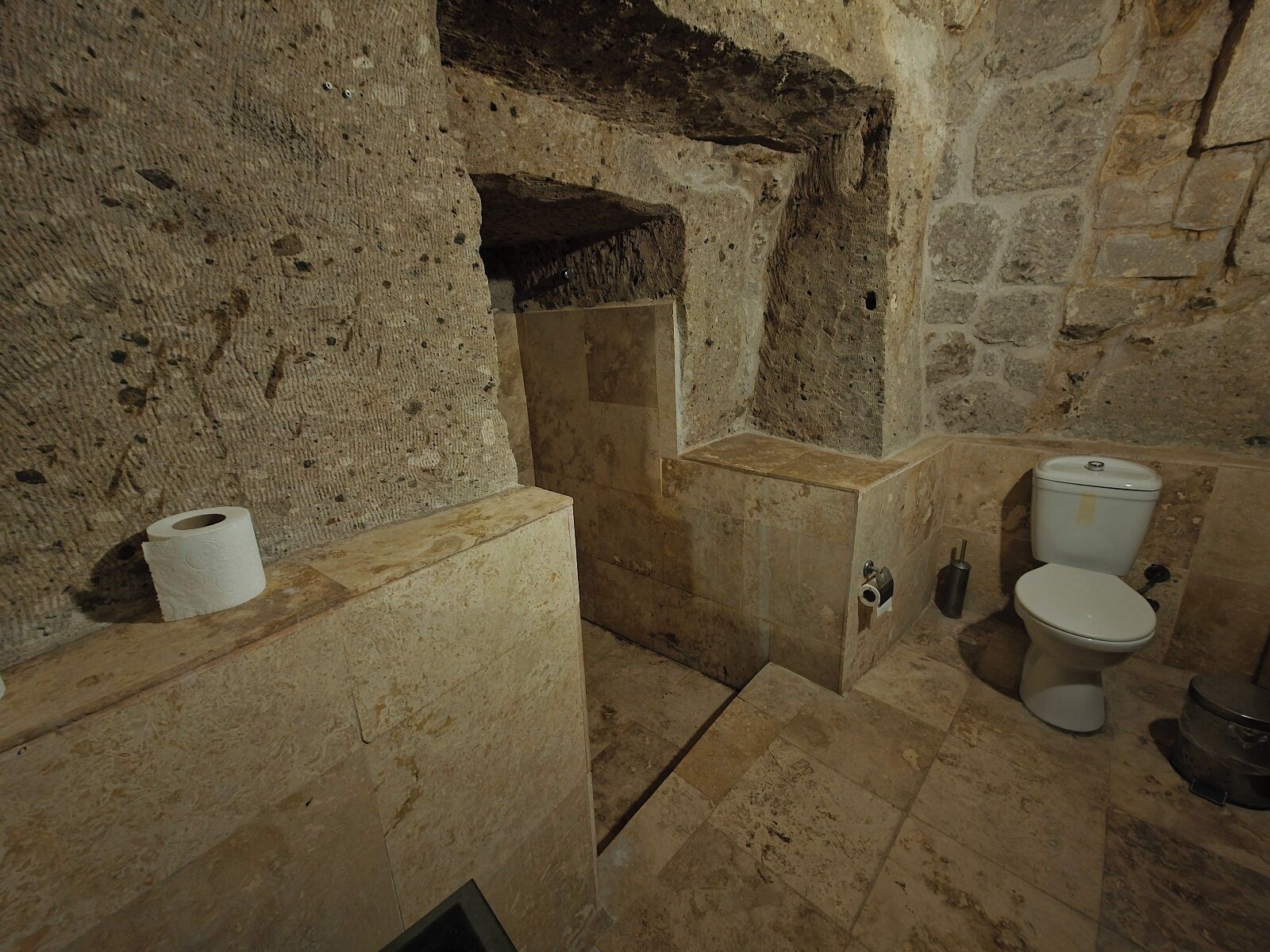Un bagno con pareti in pietra, dotato di WC, lavandino e zona doccia.