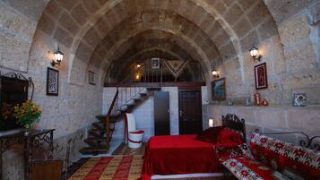 A room with a stone arch ceiling, a bed with a red bedspread, a wooden bench, and a staircase leading to an upper level.