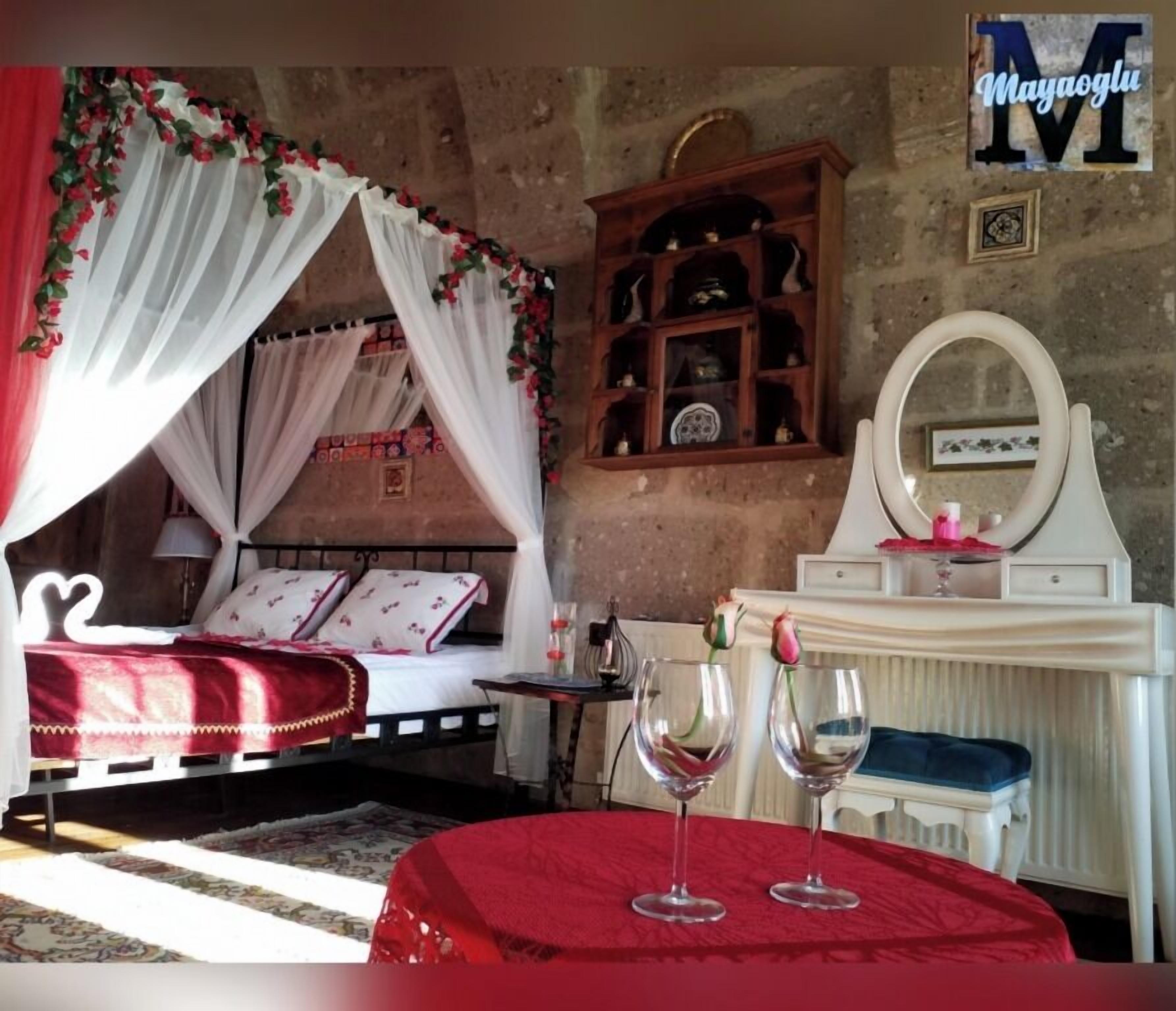Un dormitorio con cama de dosel, un aparador de madera con objetos decorativos, un tocador con espejo y dos copas de vino sobre un mantel rojo.