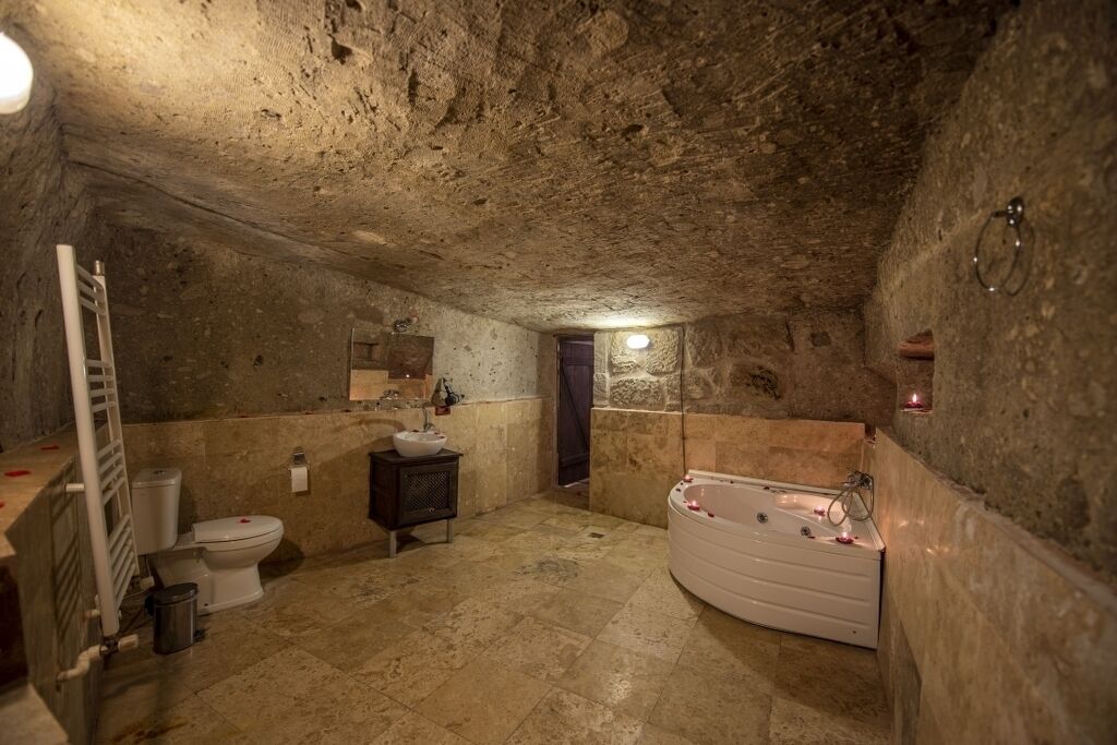 A stone-walled bathroom with a bathtub, toilet, and sink.
