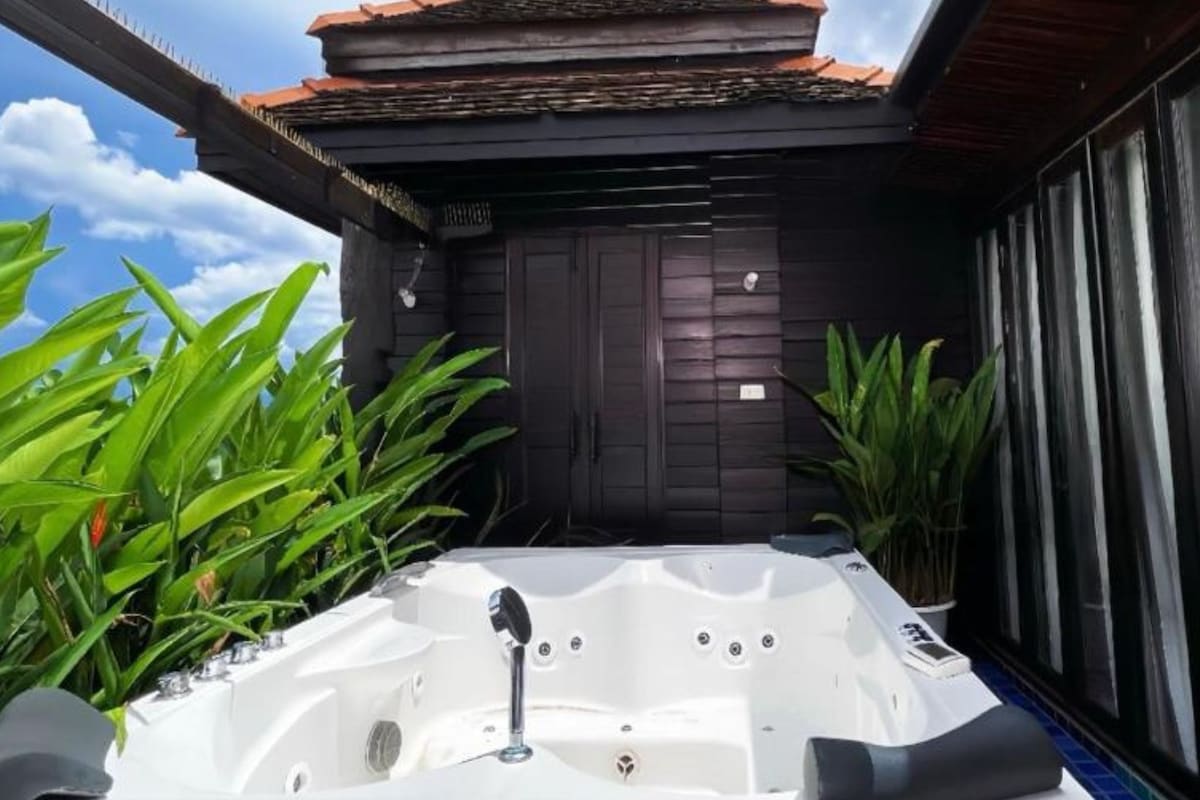 A hot tub with a wooden roof and dark siding, surrounded by lush green plants.