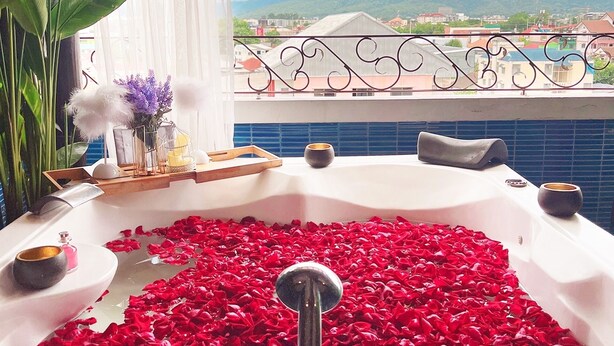 Un bain à remous rempli de pétales de rose, agrémenté d’objets décoratifs et offrant une vue sur un paysage montagneux.