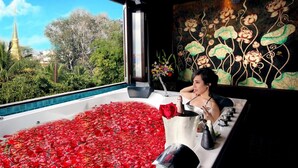 A bathtub filled with rose petals and a rose, with a view of a temple and greenery outside.