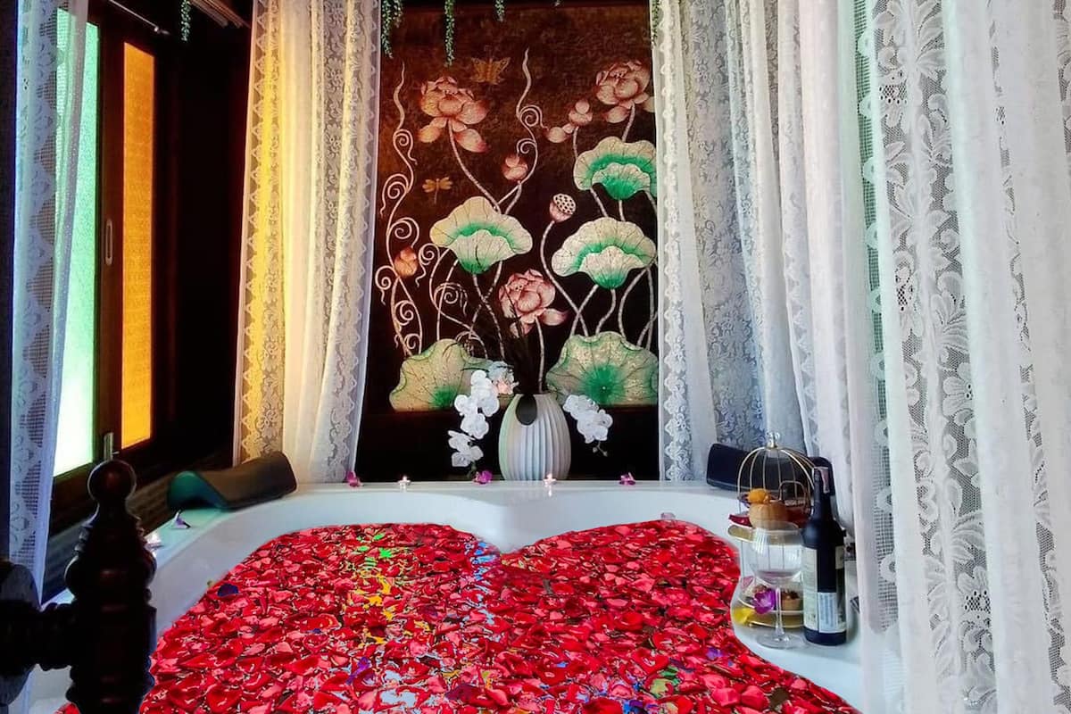Une salle de bain avec une baignoire recouverte de pétales de roses, un tableau décoratif au mur et un vase rempli de fleurs.