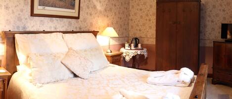 Un lit bien fait, avec une literie à motifs floraux, une table de chevet avec une lampe, une armoire en bois et un téléviseur posé sur un meuble.