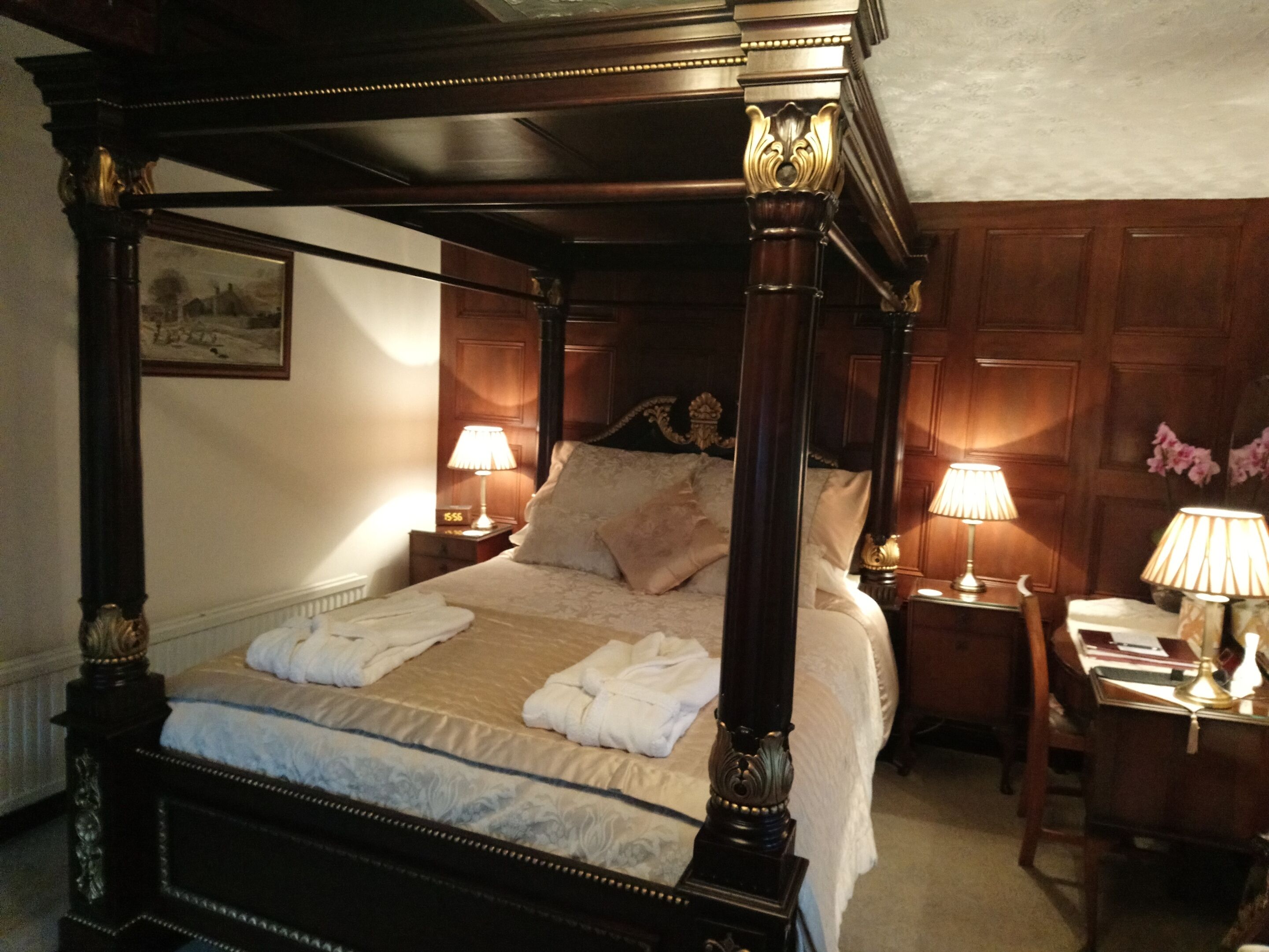 Una cama con dosel, ropa de cama y toallas blancas, dos mesitas de noche con lámparas y un cabecero de madera.