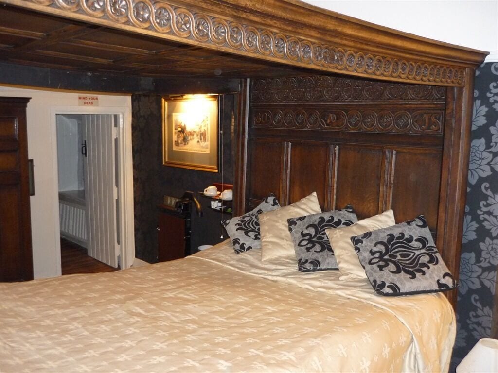 Een slaapkamer met een groot bed, een houten hoofdeinde en een deur met een bordje.