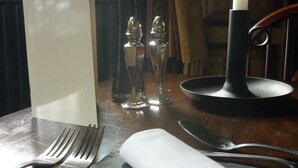 Una mesa dispuesta con una carta de vinos, saleros, pimenteros, una vela y cubiertos.