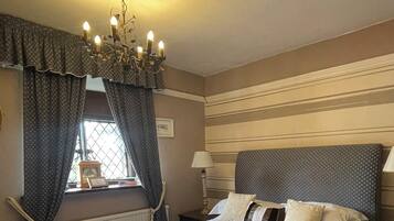 Una habitación de hotel con cama, candelabro, cortinas, ventana y mesita de noche.
