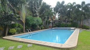A rectangular swimming pool with a stone border, surrounded by a well-maintained lawn and various tropical plants. - Tagaytay Wingate Manor (Tagaytay)