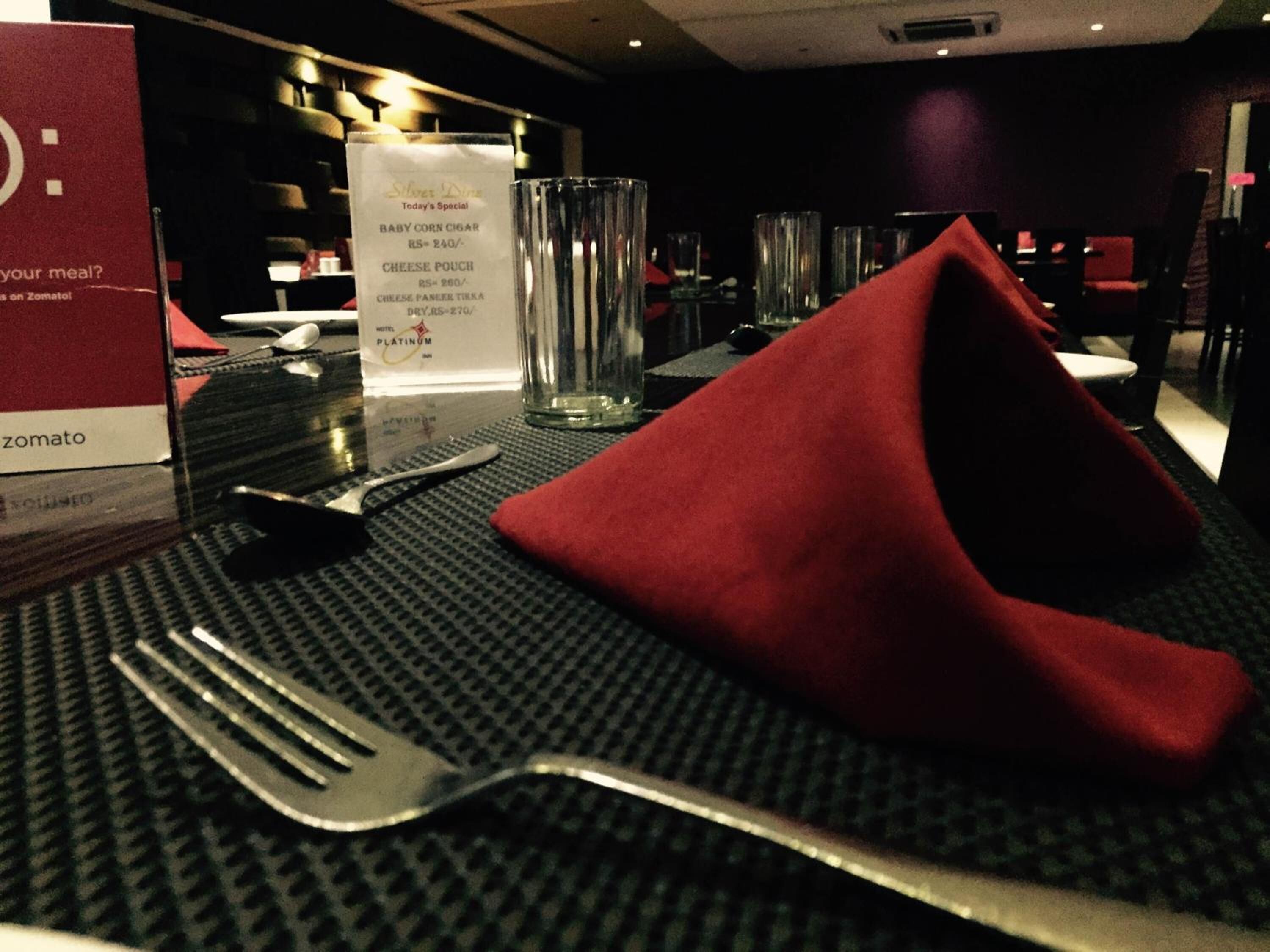 A hotel room with a dining table set for two, including a menu, a glass of water, and a red napkin.