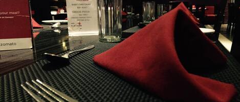 A hotel room with a dining table set for two, including a menu, a glass of water, and a red napkin.