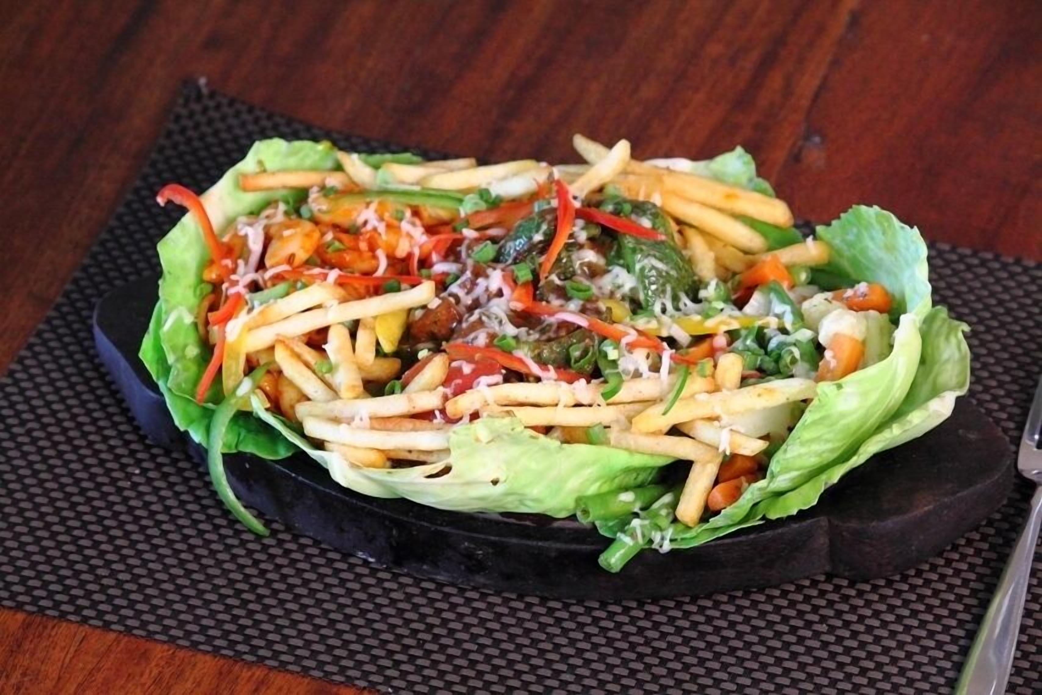 A salad with lettuce, cheese, and vegetables on a black plate.