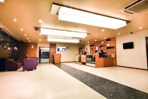 A hotel reception area with a reception desk, seating area, and a television screen. - Hotel Platinum Inn (Ahmedabad)
