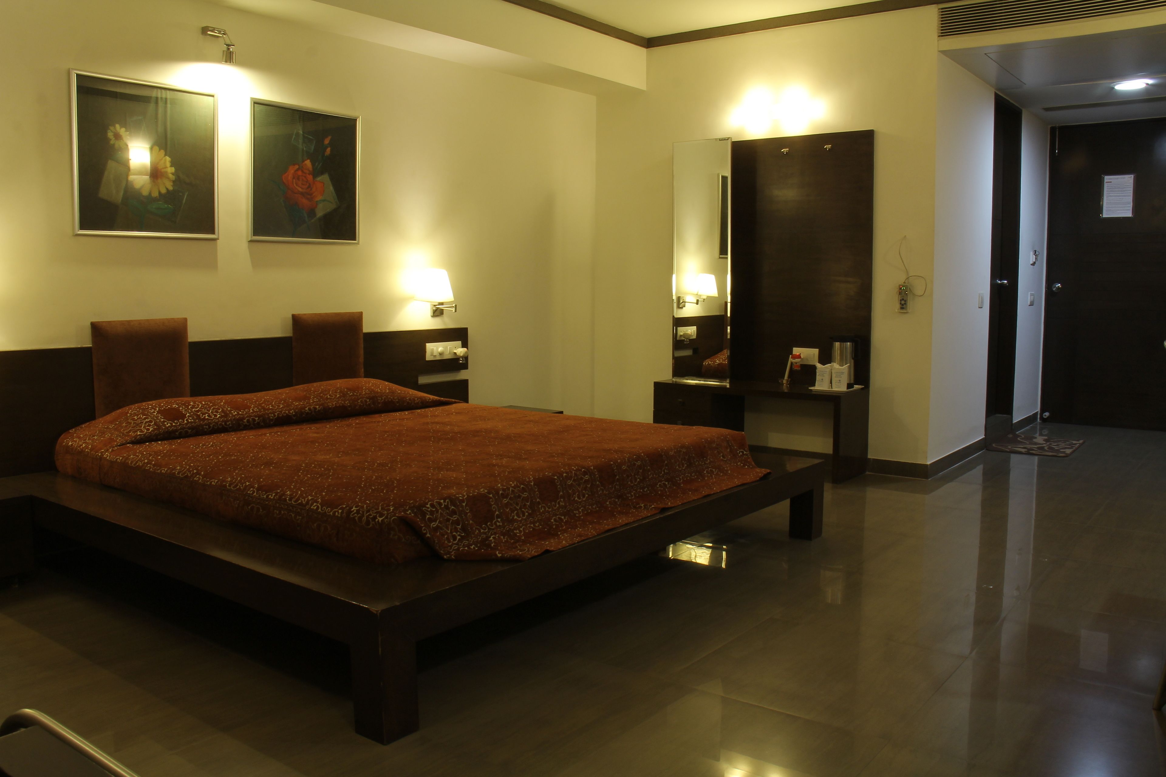 A hotel room with a large bed, bedside tables, a mirror, and wall-mounted lamps.