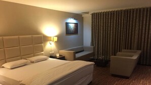 A hotel room with a large bed, a sofa, a chair, a small table, and a wall-mounted lamp. - Hotel Platinum Inn (Ahmedabad)