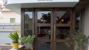 A coffee shop with a modern entrance, potted plants, and a clear sign above the door. - Hotel Platinum Inn (Ahmedabad)