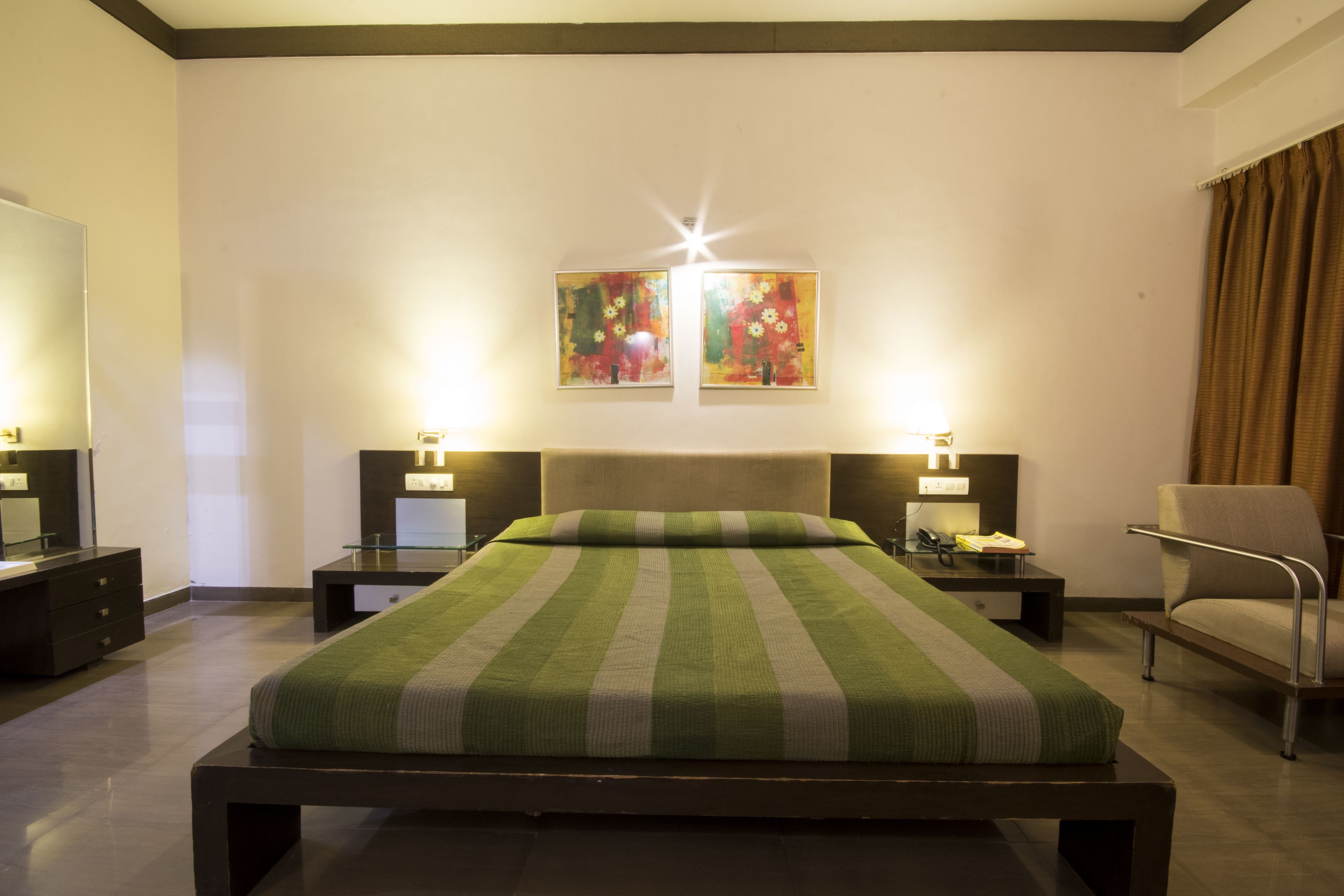 A modern hotel room with a large bed, two bedside tables, a chair, and artwork on the wall.