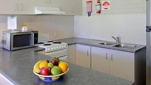 A kitchen with a microwave, stove, sink, and a bowl of fruit on the counter. - Main Beach Apartments (Byron Bay)