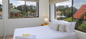 A hotel room with a large bed, a nightstand with a lamp, and a view of a tropical landscape.