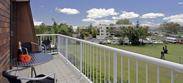 A balcony with a table and chairs, overlooking a parking area and buildings.