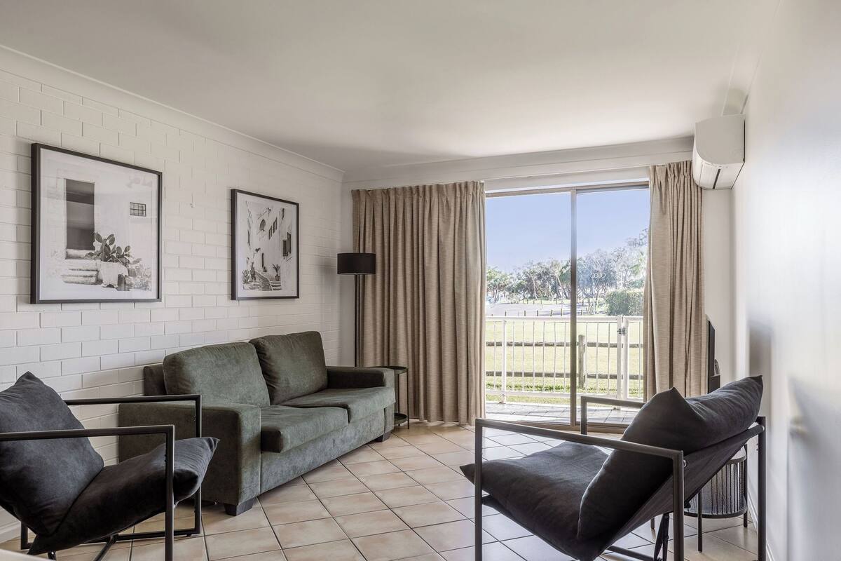 A modern living room with a green sofa, two armchairs, and a large window with curtains.