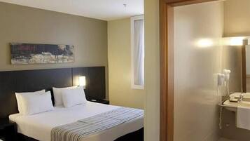 A hotel room with a large bed, a bedside lamp, a painting on the wall, and a bathroom with a sink and mirror.
