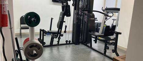 Un gimnasio con equipo de levantamiento de pesas, una prensa de banca y una cinta de correr.