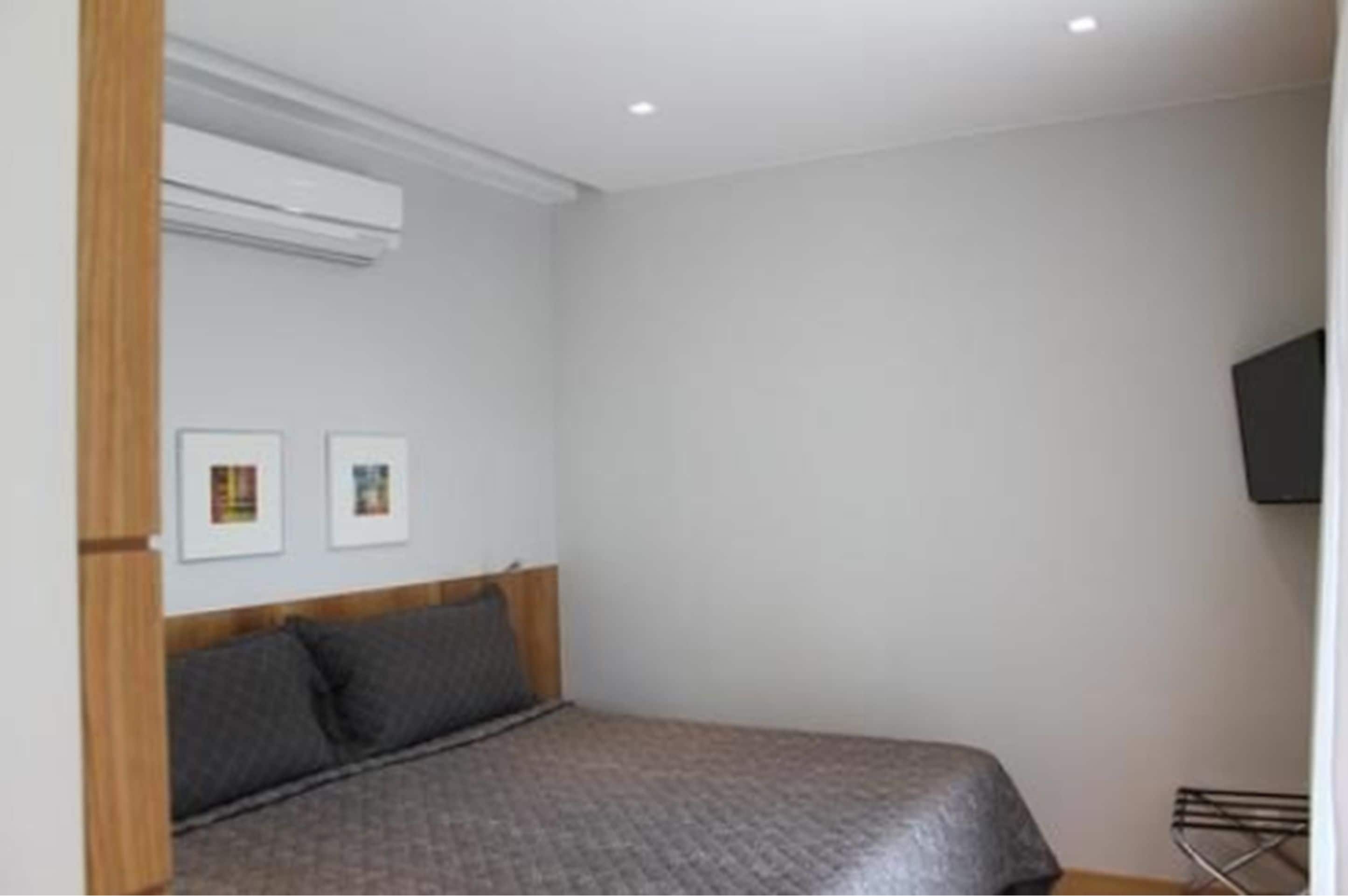 Een slaapkamer met een bed, een aan de muur bevestigde televisie en ingekaderde foto's.
