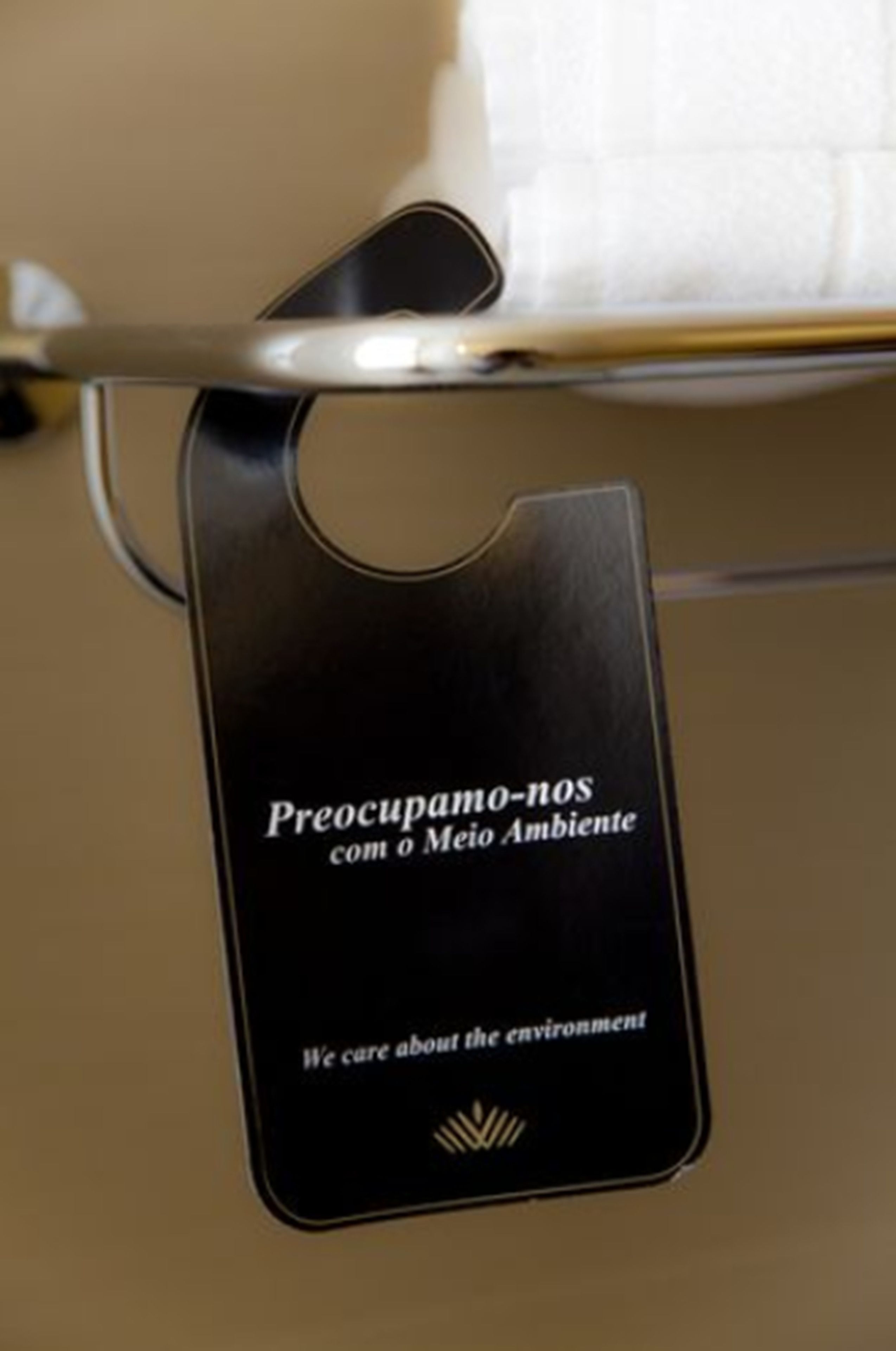 A black tag with text in Portuguese and English, attached to a metal fixture in a room.