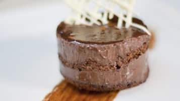 Un postre sobre un plato blanco, con base de chocolate y decoración blanca.