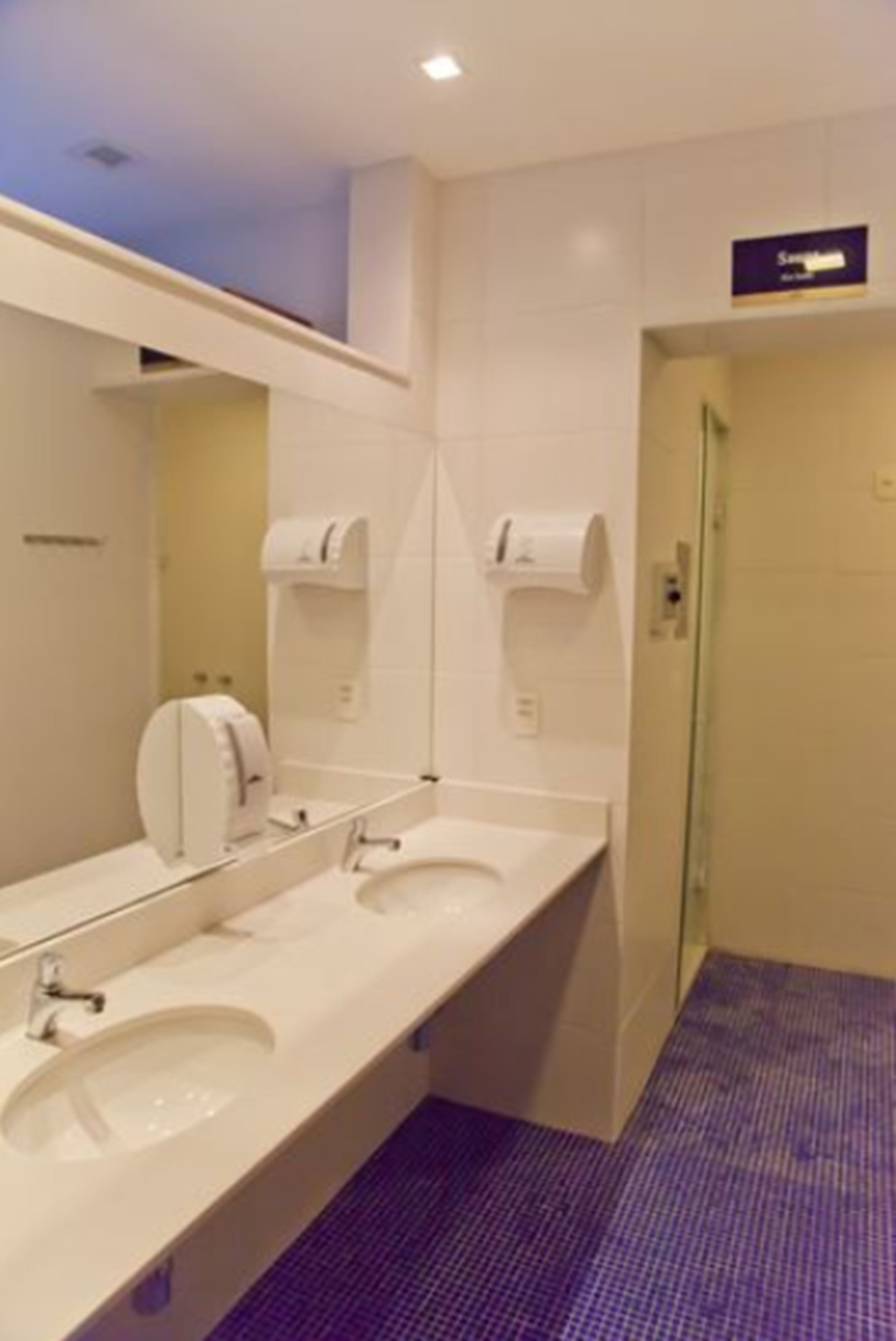 A hotel bathroom with two sinks, a large mirror, and paper towel dispensers.