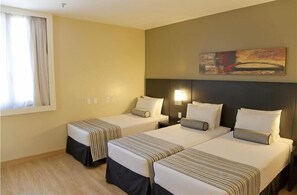 A hotel room with two beds, a large painting on the wall, and a window with curtains. - Grande Hotel Petrópolis (Petrópolis)