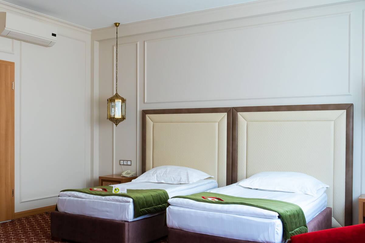 A hotel room with two beds, a wooden nightstand, a telephone, and a hanging light fixture.