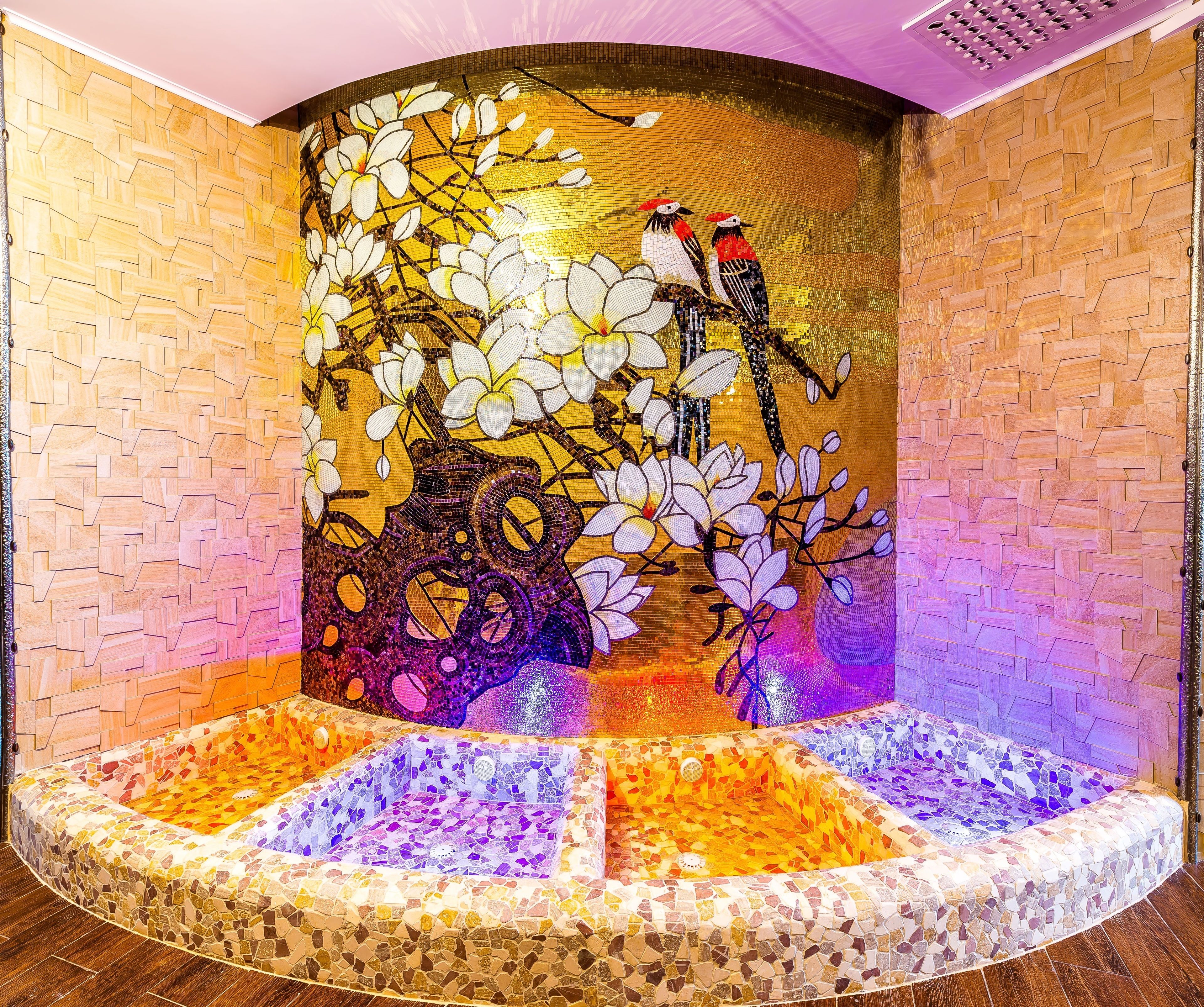 A mosaic-tiled jacuzzi with a decorative wall featuring birds and flowers.