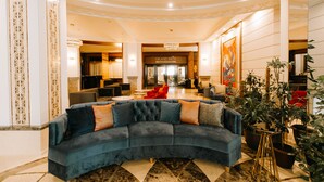 A grand lobby with a curved blue sofa, a chandelier, and a Grand Prix sign. - Jumbaktas Hotel (Astana)