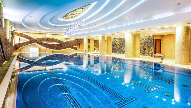 A large indoor swimming pool with a modern design, featuring a central island and a patterned wall. - Jumbaktas Hotel (Astana)