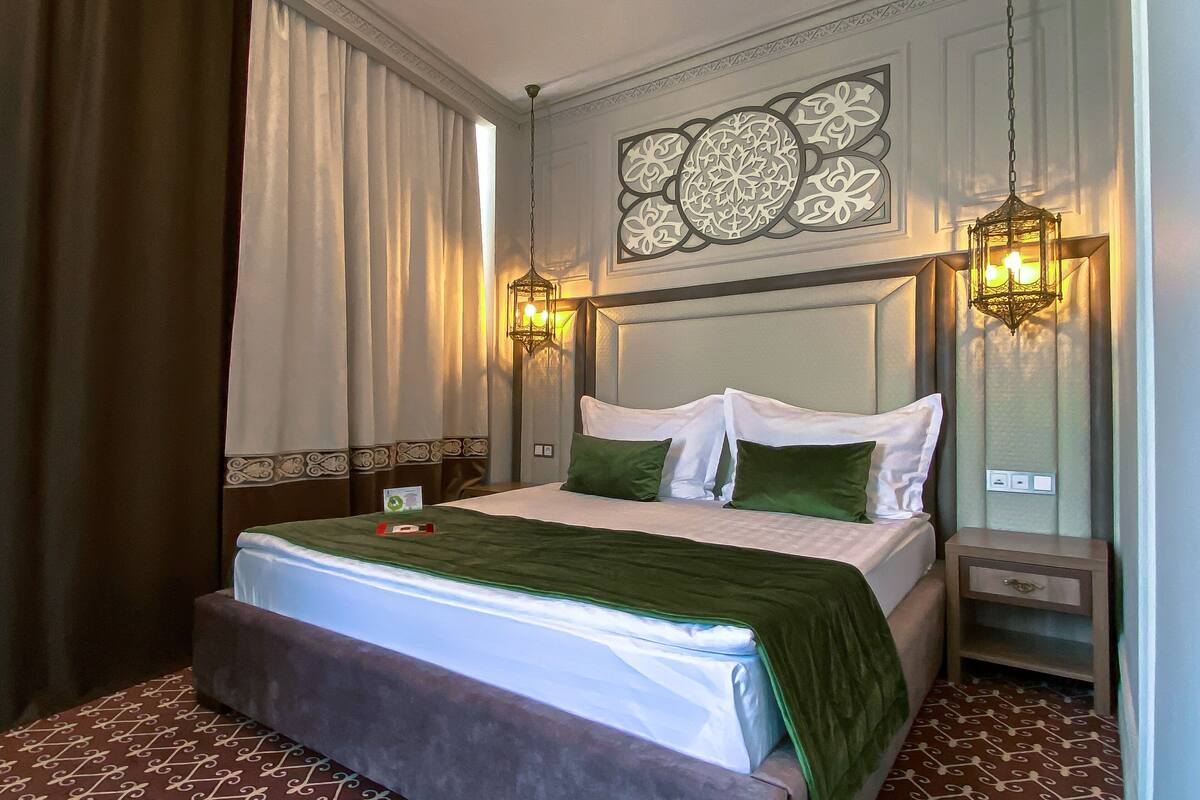 A hotel room with a large bed, two bedside tables, a decorative wall piece, and a patterned carpet.