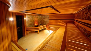 A sauna room with wooden benches, a stone wall, and a ceiling with wooden slats. - Jumbaktas Hotel (Astana)