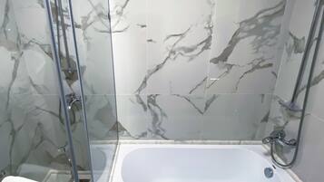 Un baño con ducha de vidrio, una bañera blanca y azulejos con diseño de mármol.