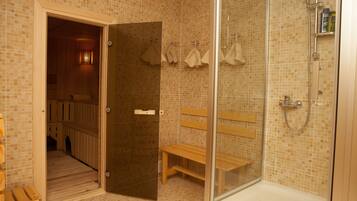 A bathroom with a glass-enclosed shower, wooden benches, and a tiled floor.