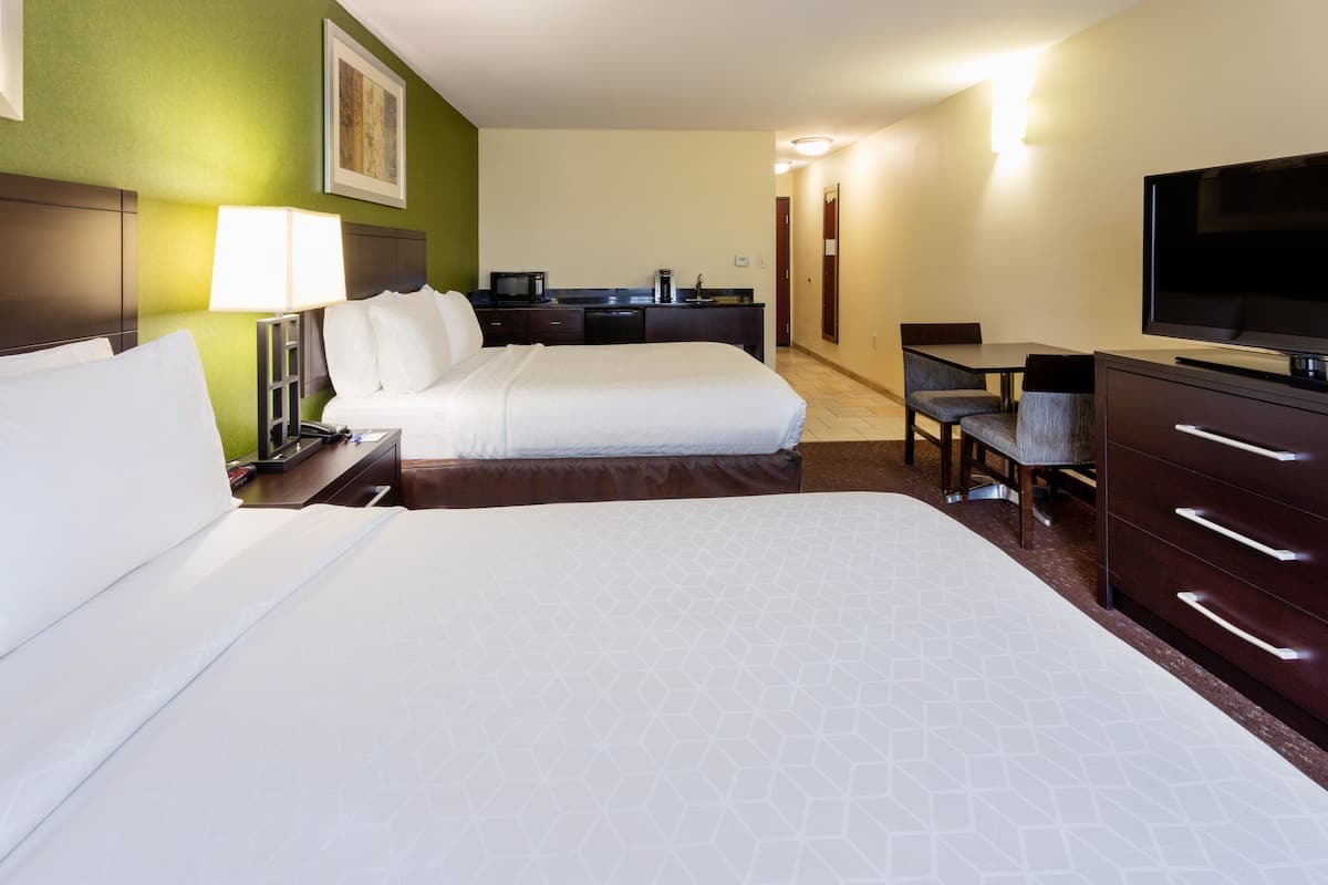 A hotel room with two beds, a desk, a chair, a television, and a kitchenette.