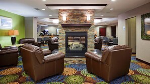 A hotel lobby with leather armchairs, a fireplace, patterned carpet, and a dining area in the background. - Holiday Inn Express & Suites Rochester – Mayo Clinic Area by IHG (Rochester)