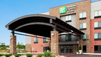 A Holiday Inn Express & Suites building with a brick facade, a covered entrance, and a clear sky.