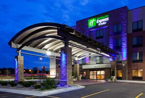 Un bâtiment de l’hôtel Holiday Inn Express doté d’une entrée couverte, d’un espace extérieur aménagé pour s’asseoir et d’une façade bien éclairée.