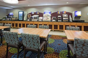 A hotel breakfast area with a self-service counter, seating, and a patterned carpet.