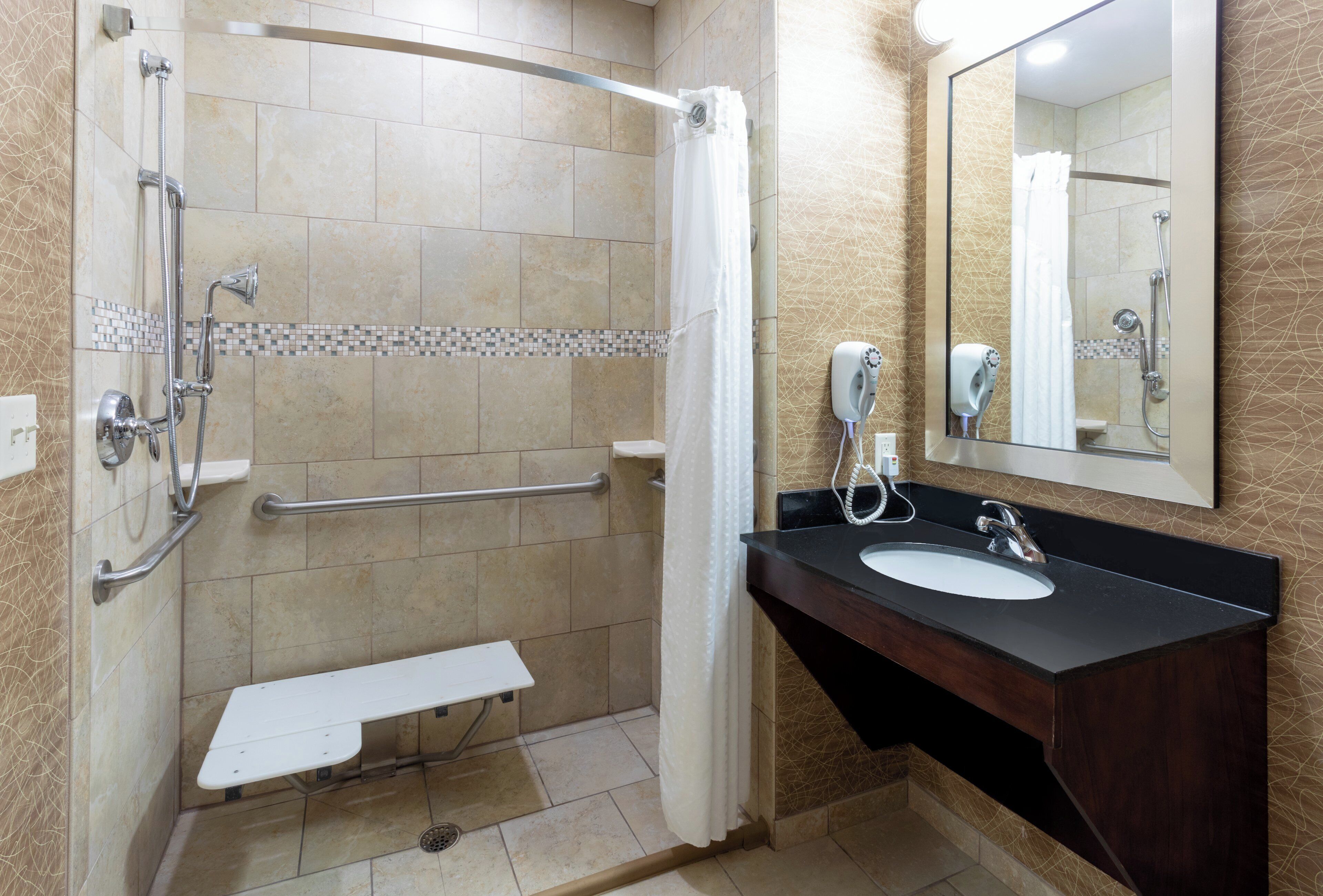 A bathroom with a shower, a sink, a mirror, and a hand dryer.